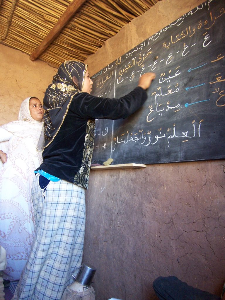 schule mellal an der tafel 2008 Eine junge Frau schreibt mit Kreide auf eine Tafel. Die Lehrerin in weißer Malifa schaut, was die Schülerin auf arabisch schreibt.
